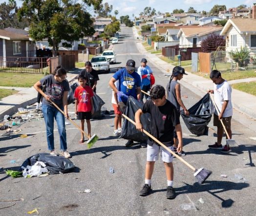 Community volunteers cleaning a neighborhood street with children participating